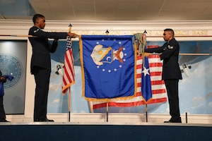 an airman unfurls a blue flag in front of another flag that is being furled behind it
