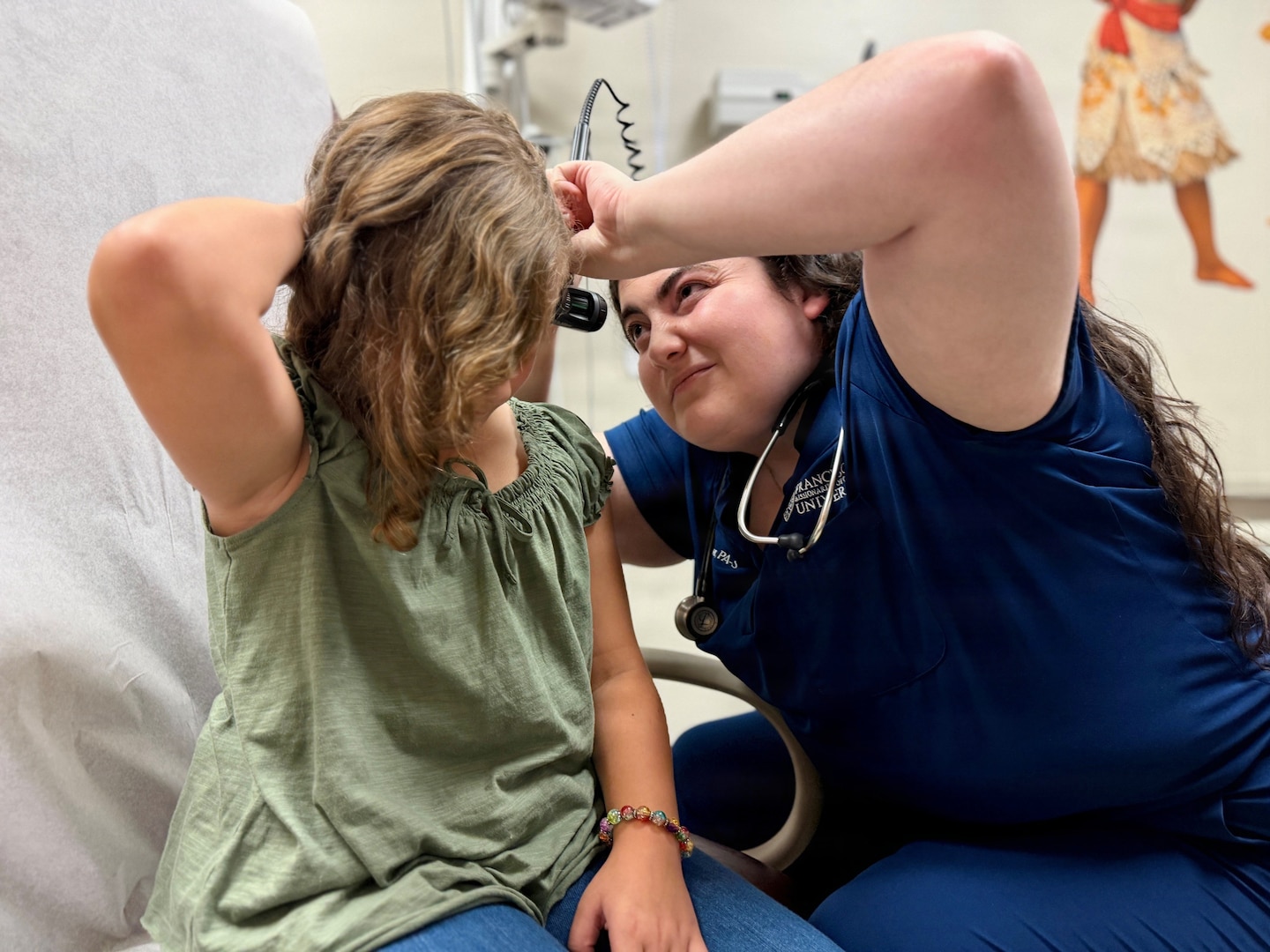 A physician assistant student examines a 9-year-old patient's ears during a pediatric clinical training encounter.