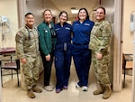Three female students in hospital garb pose with BJACH trainers in Military Uniform.