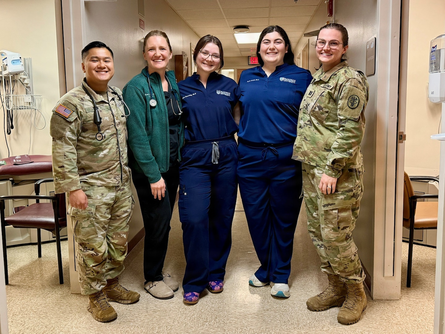 Three female students in hospital garb pose with BJACH trainers in Military Uniform.
