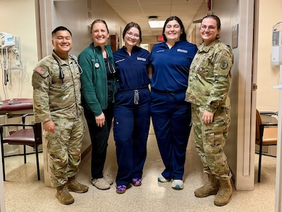 Three female students in hospital garb pose with BJACH trainers in Military Uniform.