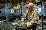 An airman collects and organizes protective bullet proof inserts in metal wire bins.