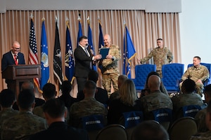William D. Bailey, preforming the duties of the Assistant Secretary of the Air Force for Acquisition, Technology and Logistics, and Brig. Gen. Joshua Williams, read the charter for Department of the Air Force Portfolio Acquisition Executive for Command, Control, Communications and Battle Management personnel and guests during a change of leadership ceremony, here, Aug. 28. Williams officially assumed leadership of DAF PAE C3BM on July 31, 2026. The PAE integrates the C3BM materiel enterprise within the department, aligning technical architecture and acquisition authorities to streamline the delivery of decision advantage capabilities via the DAF Battle Network. (Official Air Force Photo by Richard Blumenstein).