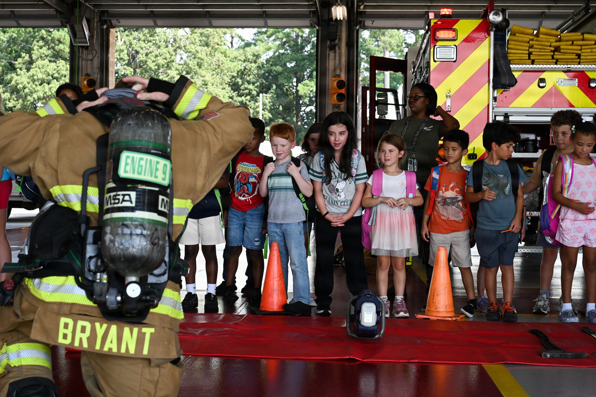 Military children watching an Airmen put on firefighter gear.