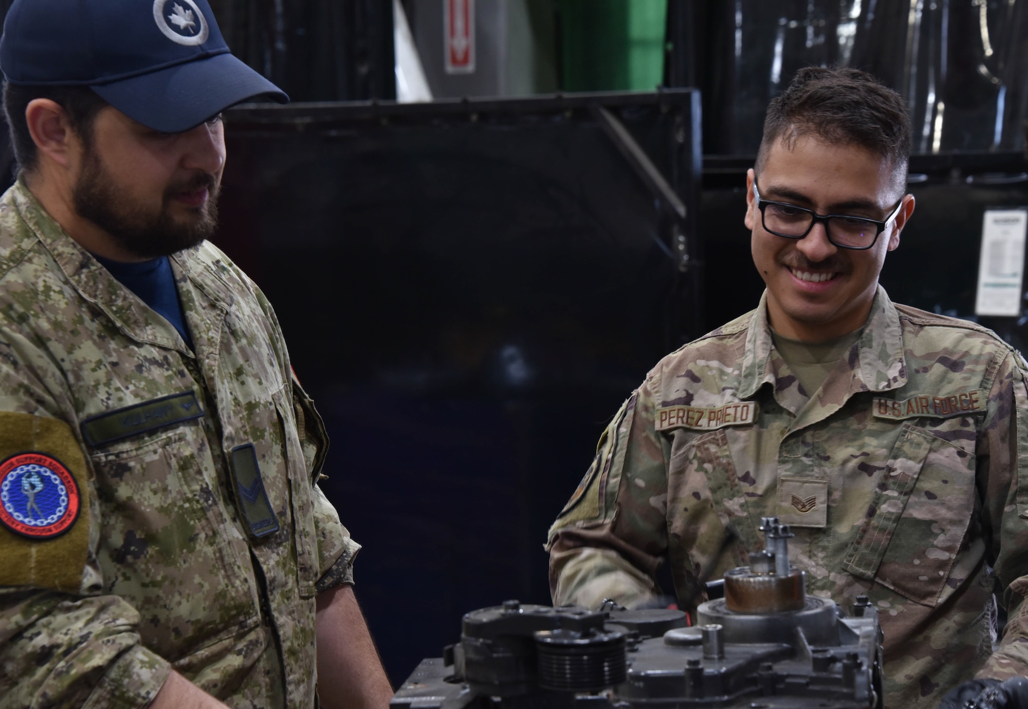 Royal Canadian Air Force Cpl. Jonathan Kulhawy, a 4-Wing electrical generating systems technician, left, and U.S. Air Force Staff Sgt. Hector Perez-Prieto, a 185th Civil Engineering Squadron electrical power production specialist, Iowa National Guard, right, look at an engine