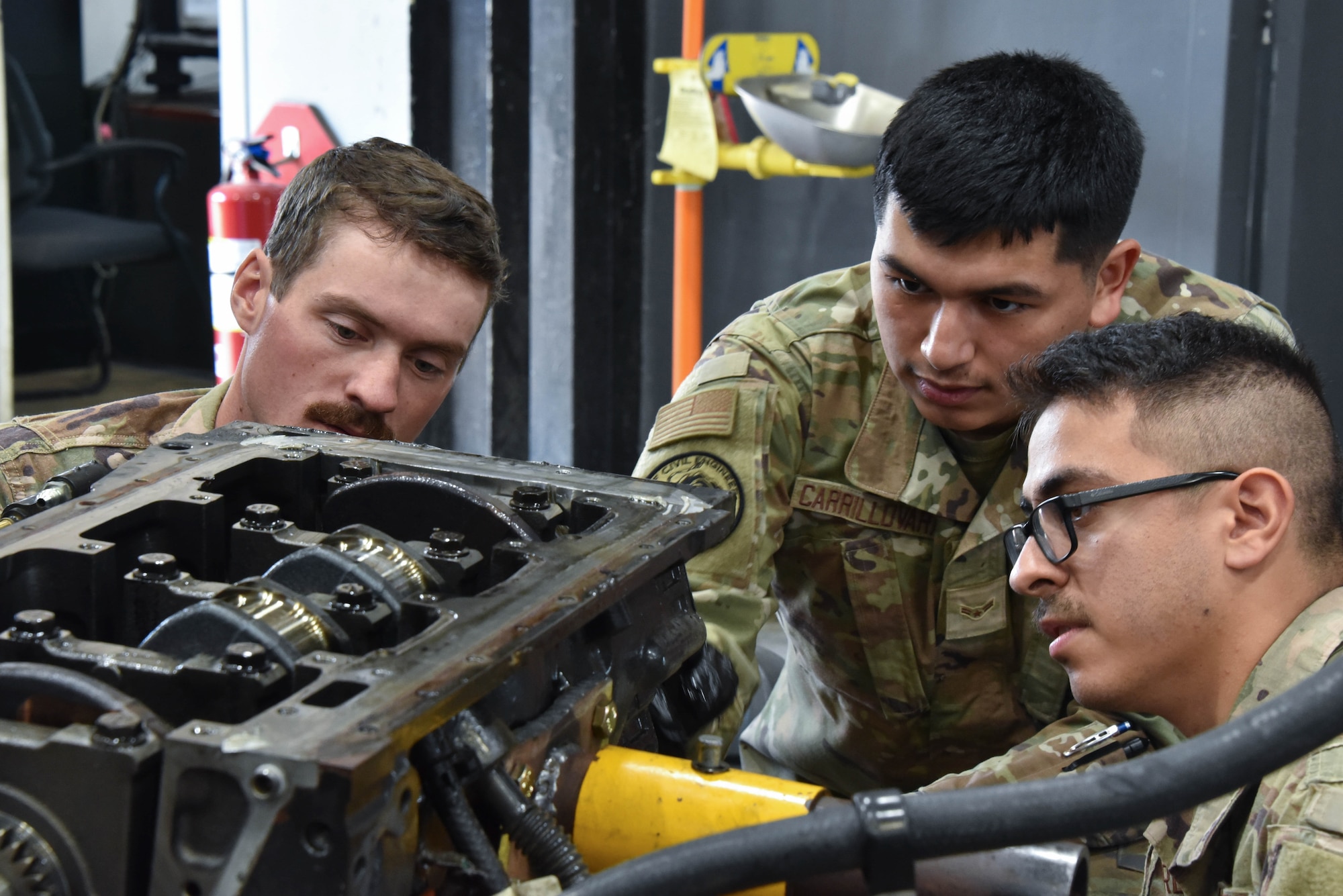 Staff Sgt. Nicholas Nielson, a 185th Civil Engineering Squadron electrical power production specialist, Iowa National Guard, left, Airman 1st Class Adrian Carrillovara, a 185th CES electrical power production specialist, center and Staff Sgt. Hector Perez-Prieto, a 185th CES electrical power production specialist, right, squat around an engine