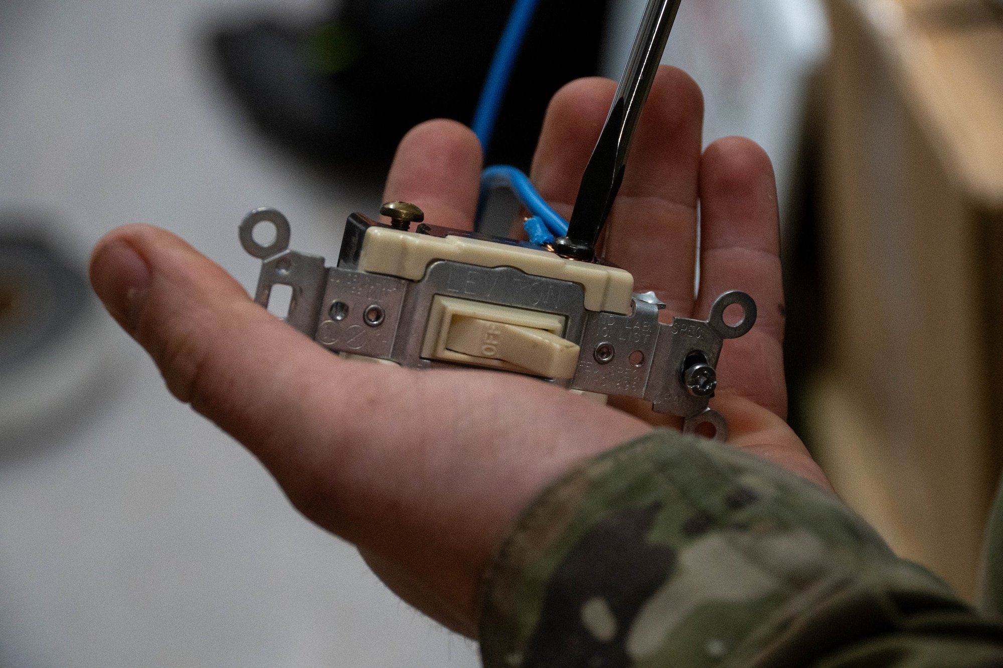 An Airman works on a light switch with a screwdriver in his palm