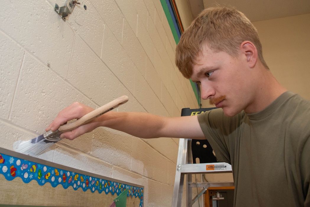 Airman 1st Class Jackson Williams paints around a bulletin board