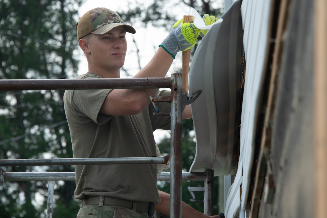 Airman 1st Class Mason Streeter pries a piece of siding with a claw hammer