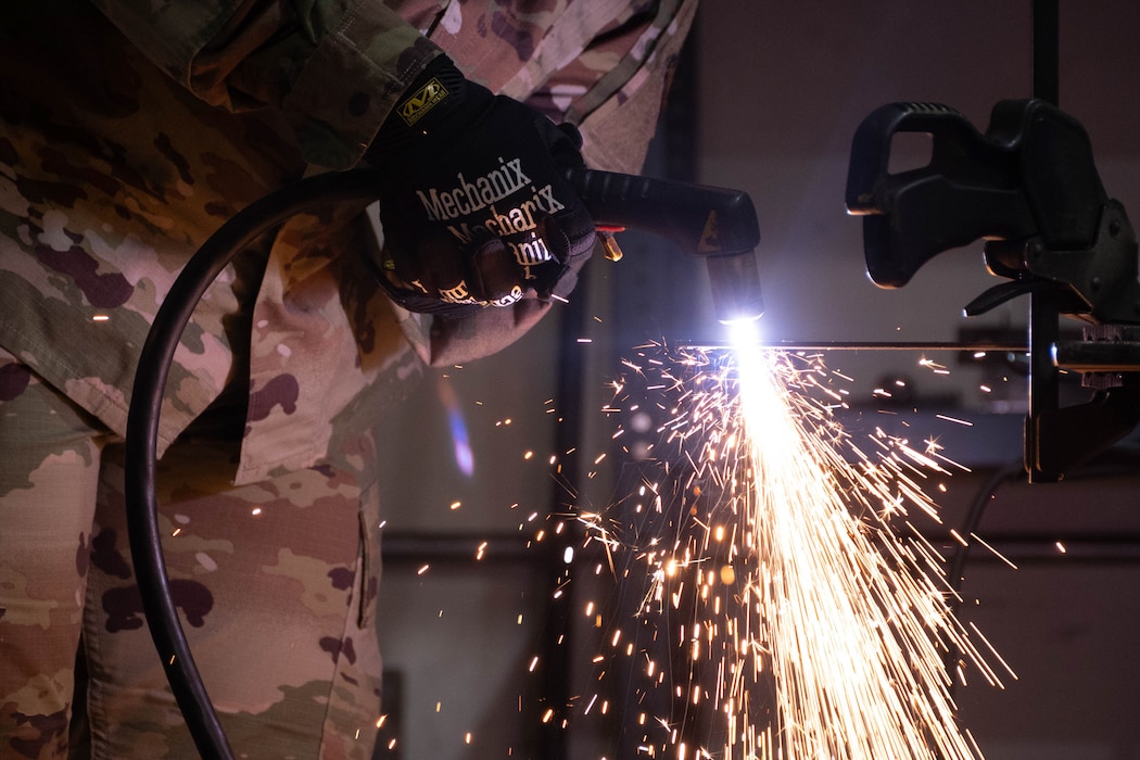 An Airman bends over and cuts with a plasma cutter