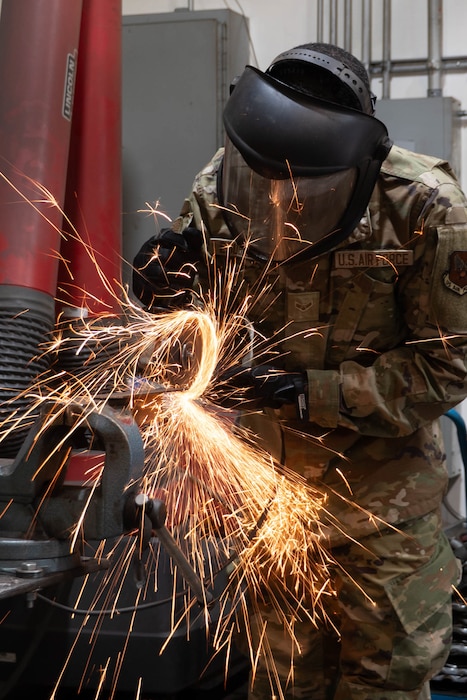 Airman 1st Class Mubarek Esubalew cuts metal with an angle grinder, sending sparks out from under the metal