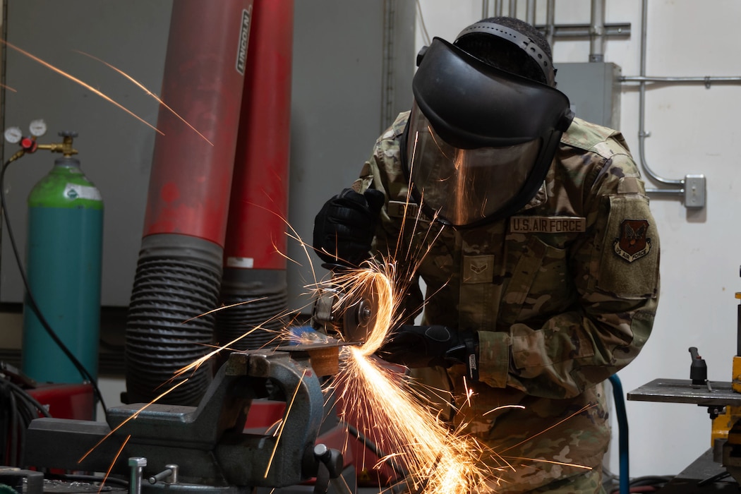 Airman 1st Class Mubarek Esubalew cuts metal with an angle grinder, sending sparks out from under the metal