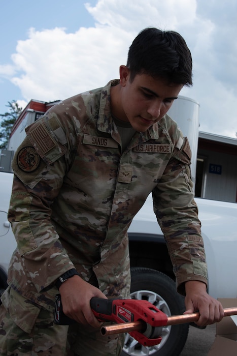 Airman 1st Class Tanner Sands cuts a copper pipe with a motorized pipe cutter