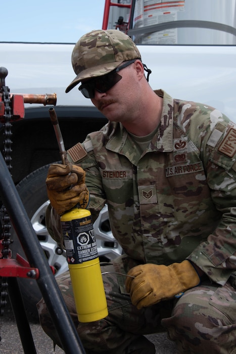 Staff Sgt Brandon Stender squats and uses a blow torch on a copper pipe