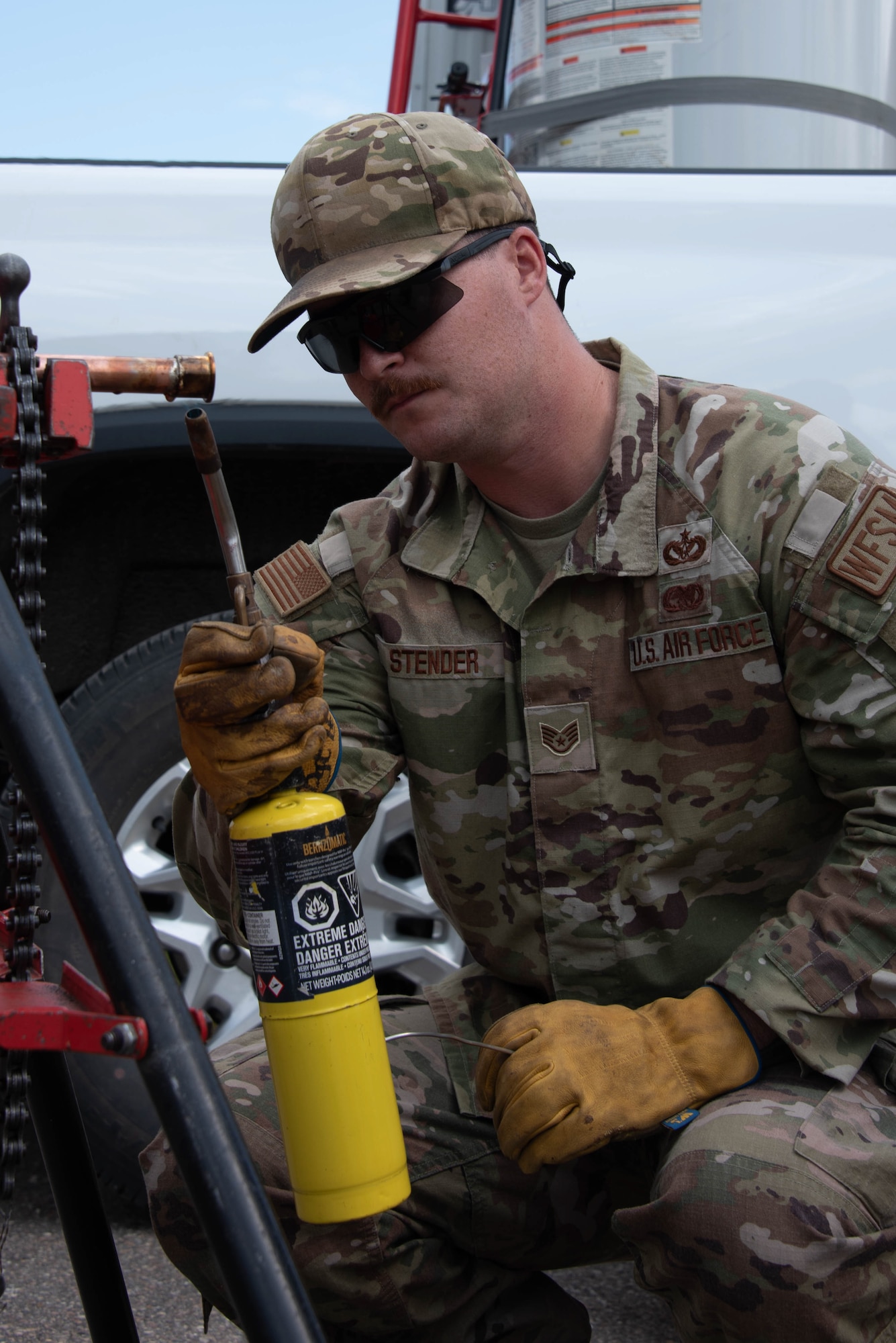 Staff Sgt Brandon Stender squats and uses a blow torch on a copper pipe