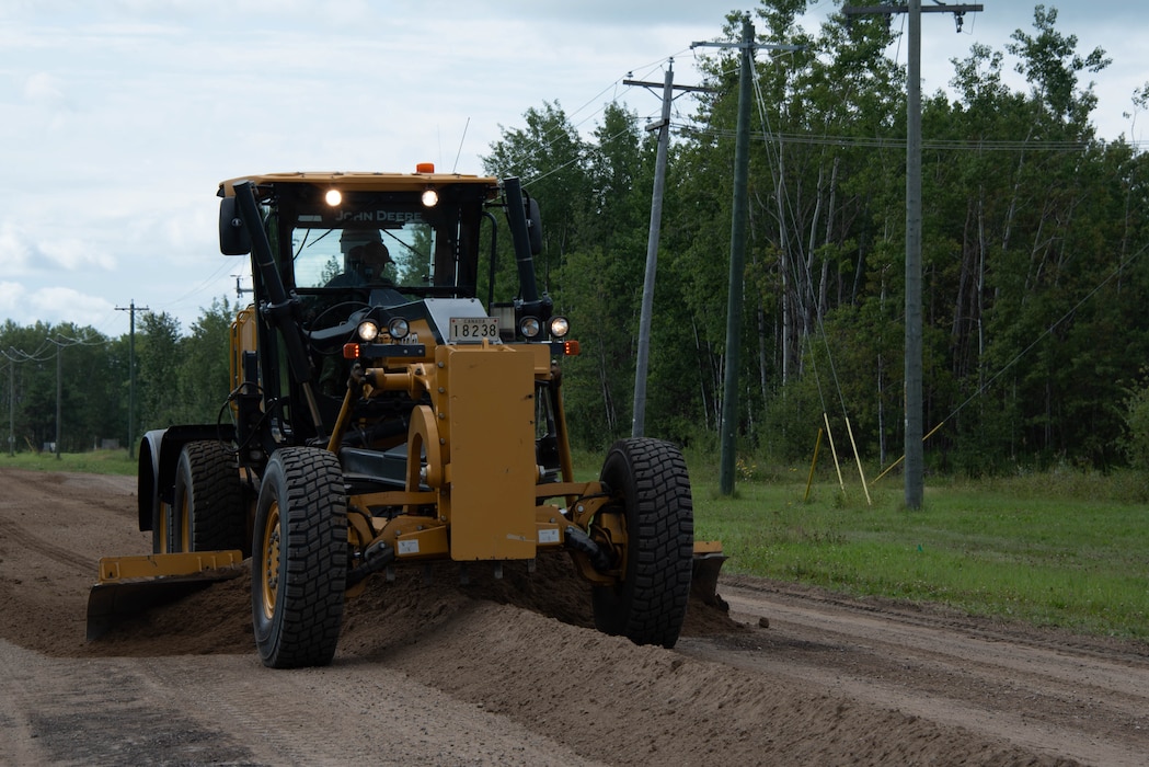 A road grader operates on a dirt road