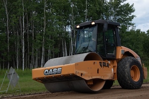 A road roller is driven on a dirt road.