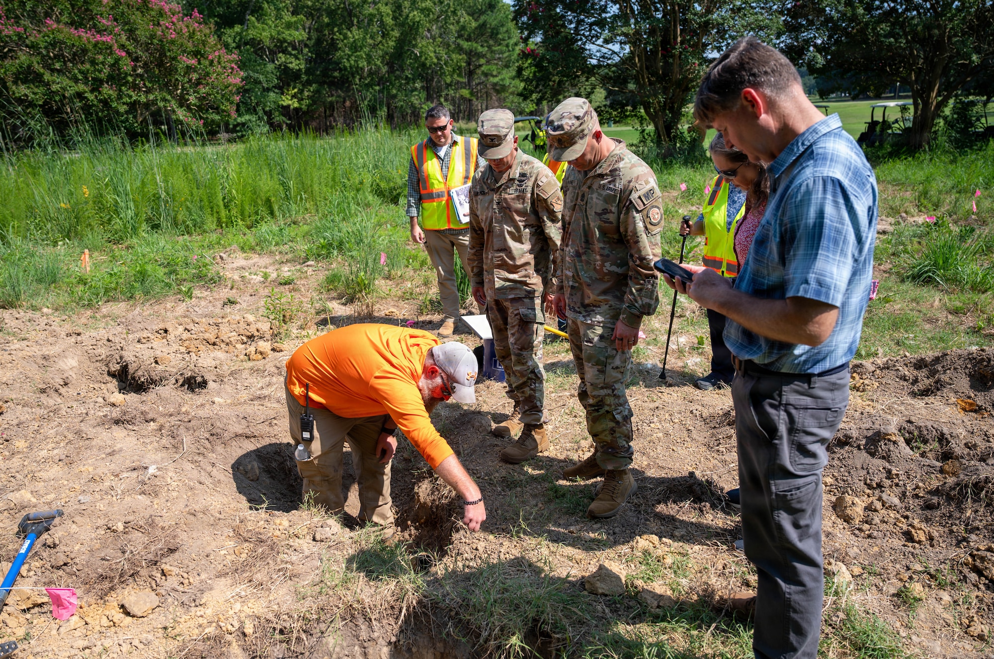 Soldiers watch a man excavate a dig site.