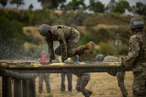 An Airman clears a log obstacle under water spray.