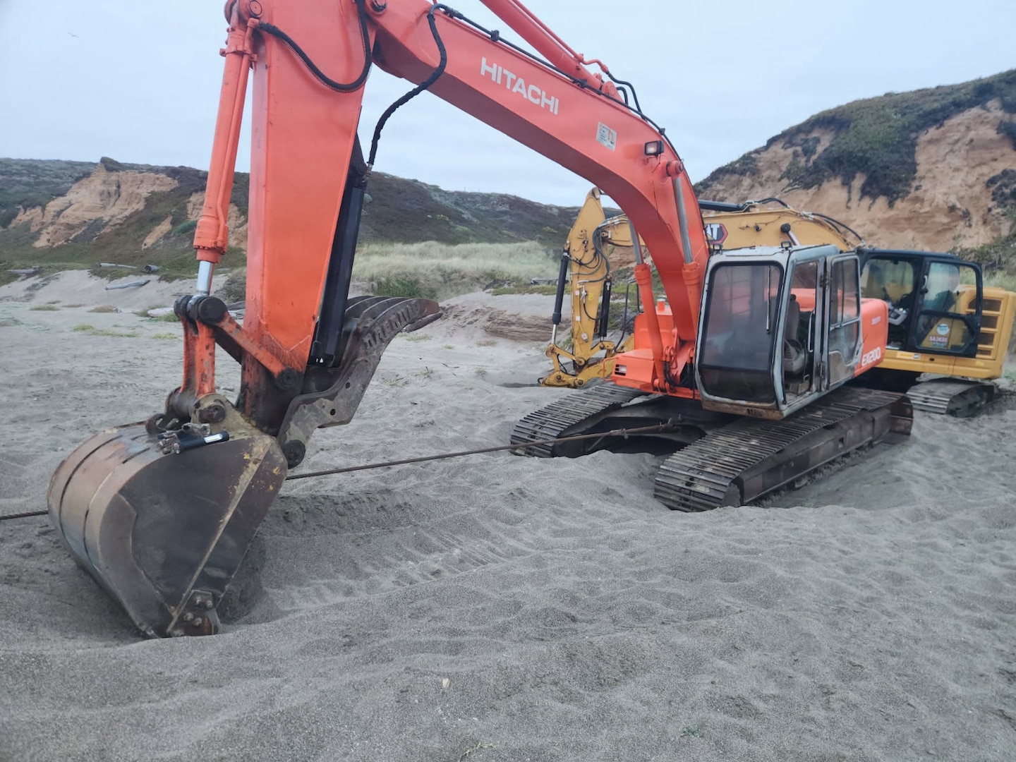 Excavators with tow lines connected to aground fishing vessel Lake Bay sit on Point Reyes North Beach, California, August 27, 2026. Due to the vessel being declared unseaworthy, response crews from the Coast Guard, National Parks Service, California Fish and Wildlife, and Parker Diving rigged the vessel’s hull with stabilization straps and tow lines for shore-based removal. (U.S. Coast Guard courtesy photo)