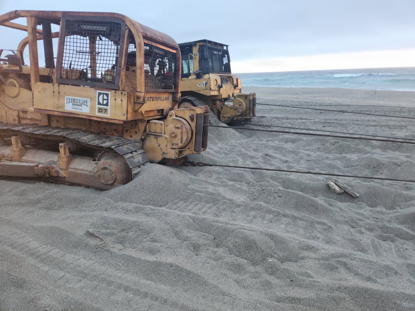 Compact tract loaders with tow lines connected to aground fishing vessel Lake Bay sit on Point Reyes North Beach, California, August 27, 2026. Response crews from the Coast Guard, National Parks Service, California Fish and Wildlife, and Parker Diving rigged the vessel’s hull with stabilization straps and tow lines for shore-based removal. (U.S. Coast Guard courtesy photo)