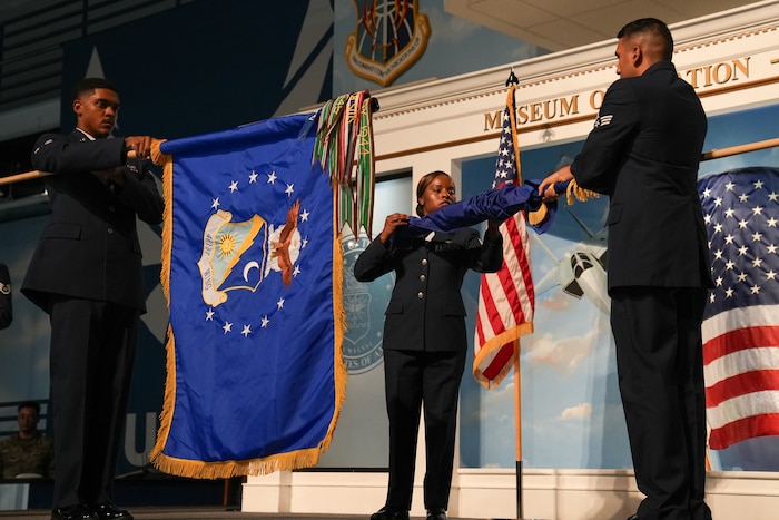 an airman holds a blue flag while standing in front of another airman holding a flag that is being sheathed by an airman