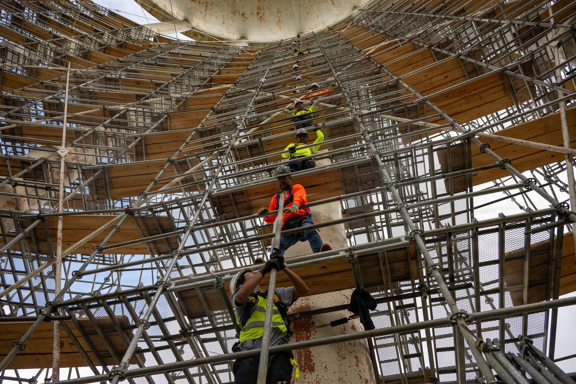 Washington Suburban Sanitary Commission contractors pass scaffolding compoments to build a path to the balcony of the water tower at Joint Base Andrews, Maryland, Aug. 5, 2026. Andrews is working with Prince George's County to preserve the rich history of the tower while repairing the worn sections of the structure. (U.S. Air Force photo by Senior Airman Alexis Redin)