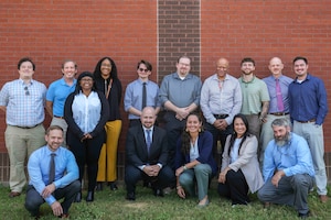 a group of 15 people pose together in front of a brick wall