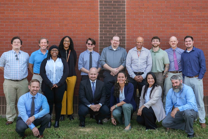 a group of 15 people pose together in front of a brick wall