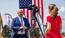 Mr. Adam Telle in front of a camera and flags