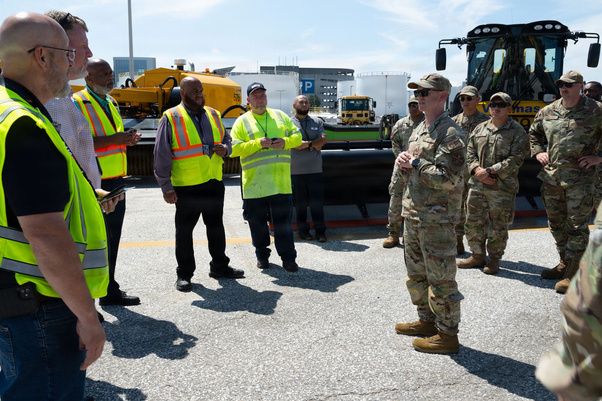 A groups of men in yellow vests stand opposite a group of men and women wearing the Air Force uniform.