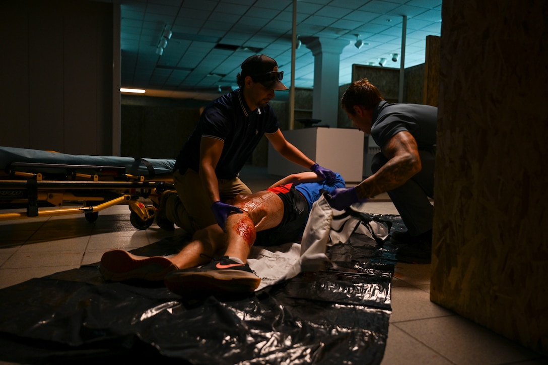 Two paramedic students assist a simulated injured patient that is lying on the ground.