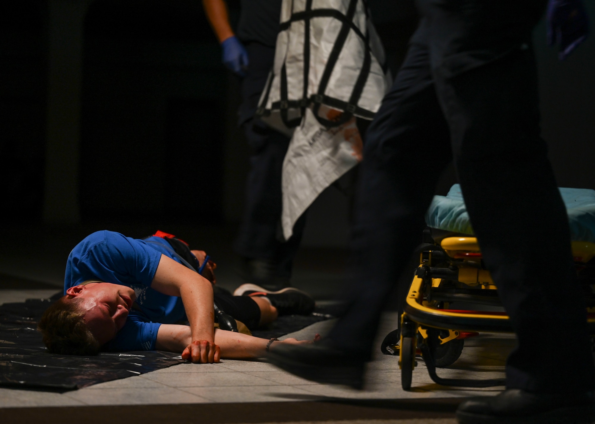 A person lays on the ground as two paramedics walk towards him.