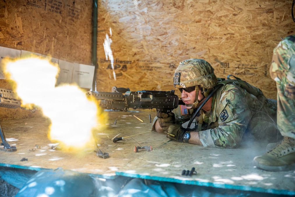 A soldier lies on a wooden board and fires a rifle straight ahead.