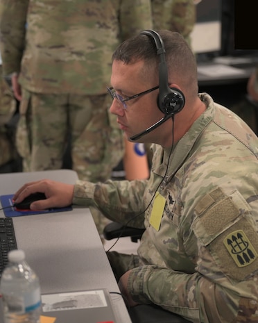 U.S. Army Soldier wearing a headset works on a computer