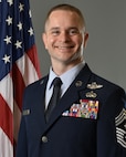 Chief Sjoholm poses for an official photo in his service dress. He is shown from the waist up with the U.S. flag over his right shoulder and a grey background.
