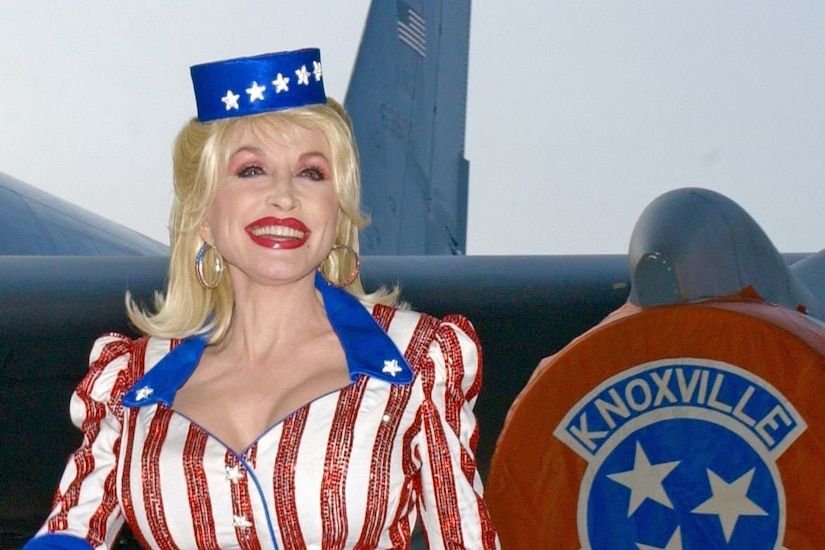 A woman in patriotic attire walks and smiles in front of a military aircraft that says, "Knoxville, Tennessee," on the wing.