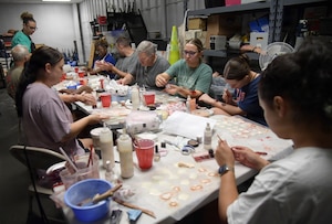 A group of people sit around of table full of moulage art supplies while applying moulage to their arms and hands.