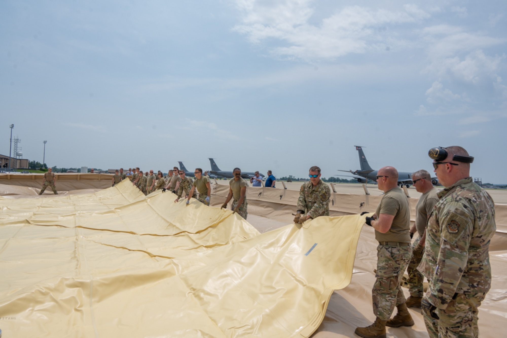 Airmen pull on large yellow plastic blatter to begin to stretch it out.
