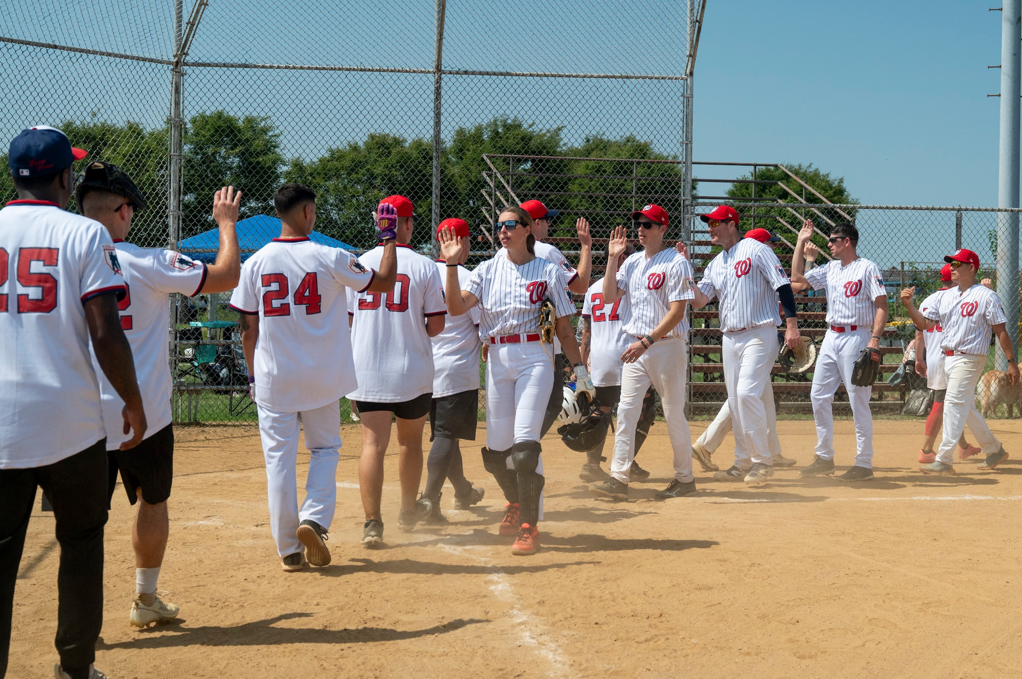 Softball players in white uniforms high-five each other as they leave the field following a game.