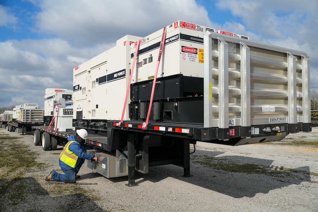 a man works on a flatbed trailer carrying generators and external fuel tanks