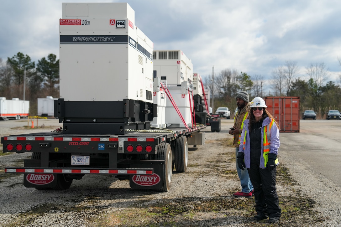 a woman stands next to a flatbed trailer loaded with generators and external fuel tanks.