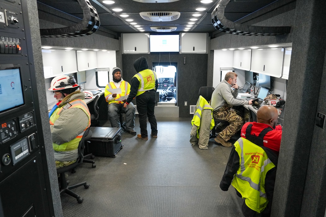people are sitting at work stations along the outer walls of a tactical operations vehicle.