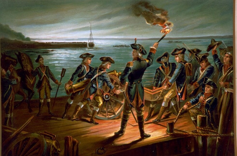 Men in military uniforms hold a cannon on a wooden boat tied to a dock in a river at night, as one of them holds a smoking torch.