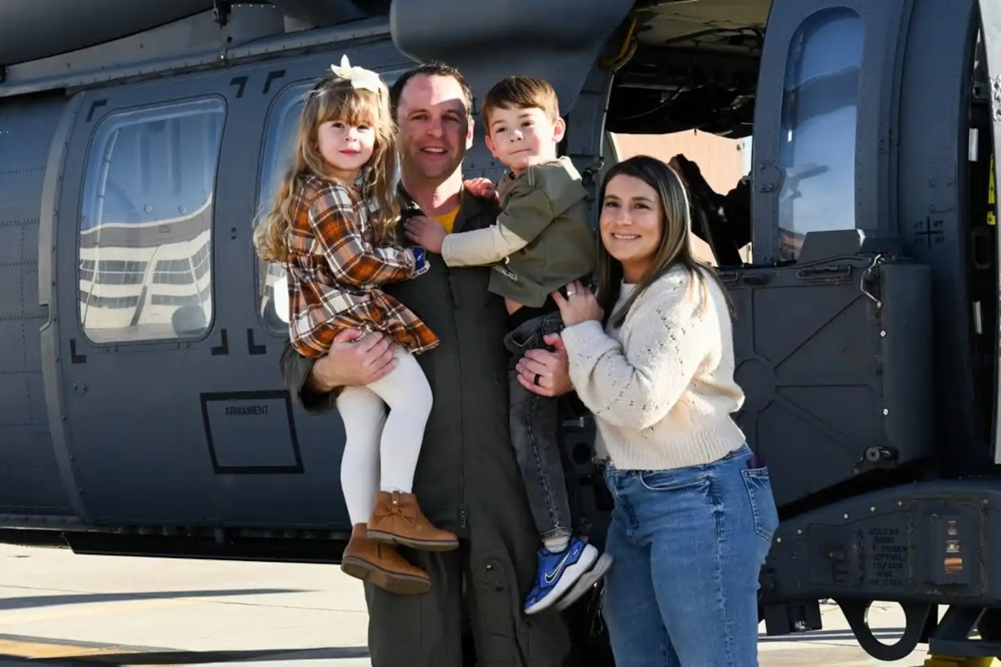 An Airman in a flight uniform stands with his family in front of a helicopter.