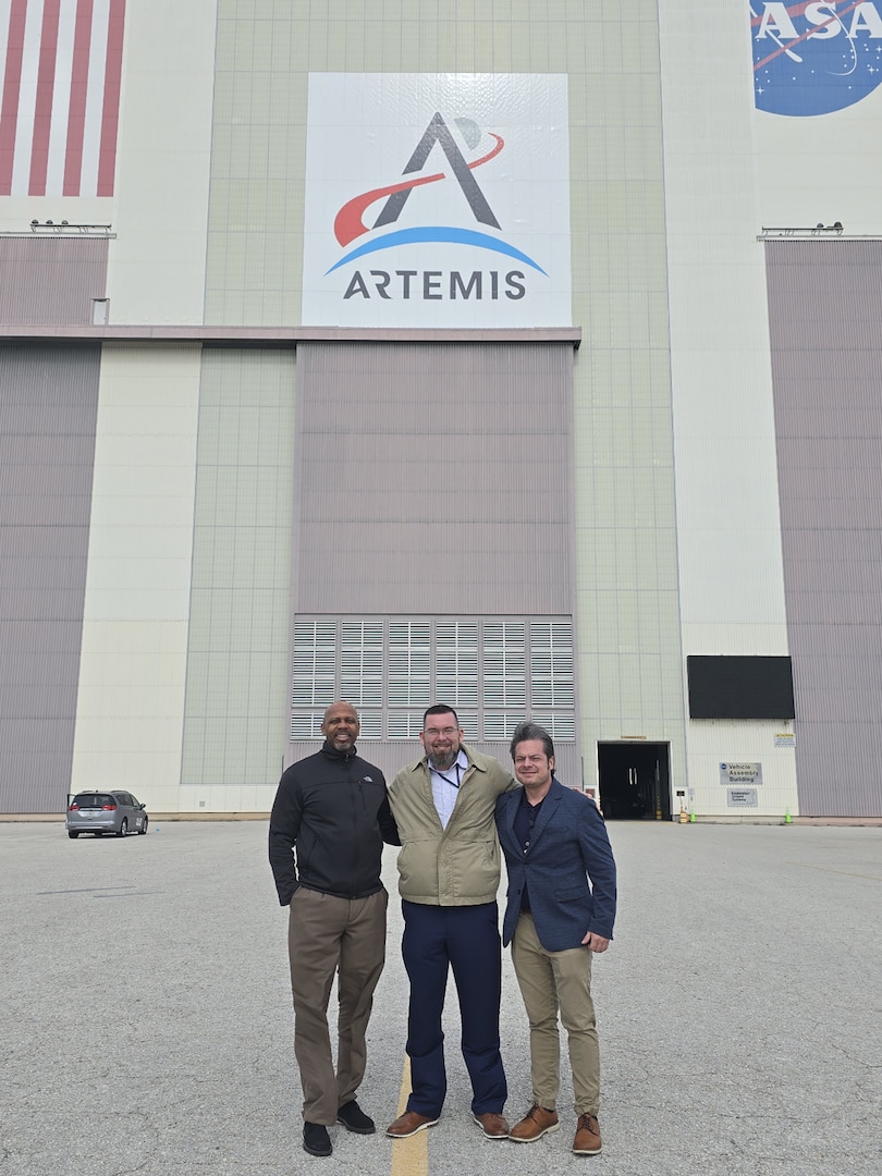 Three men stand in front of a building for a photo