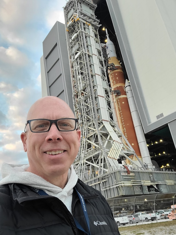 A man poses for a selfie in front of rocket ship.