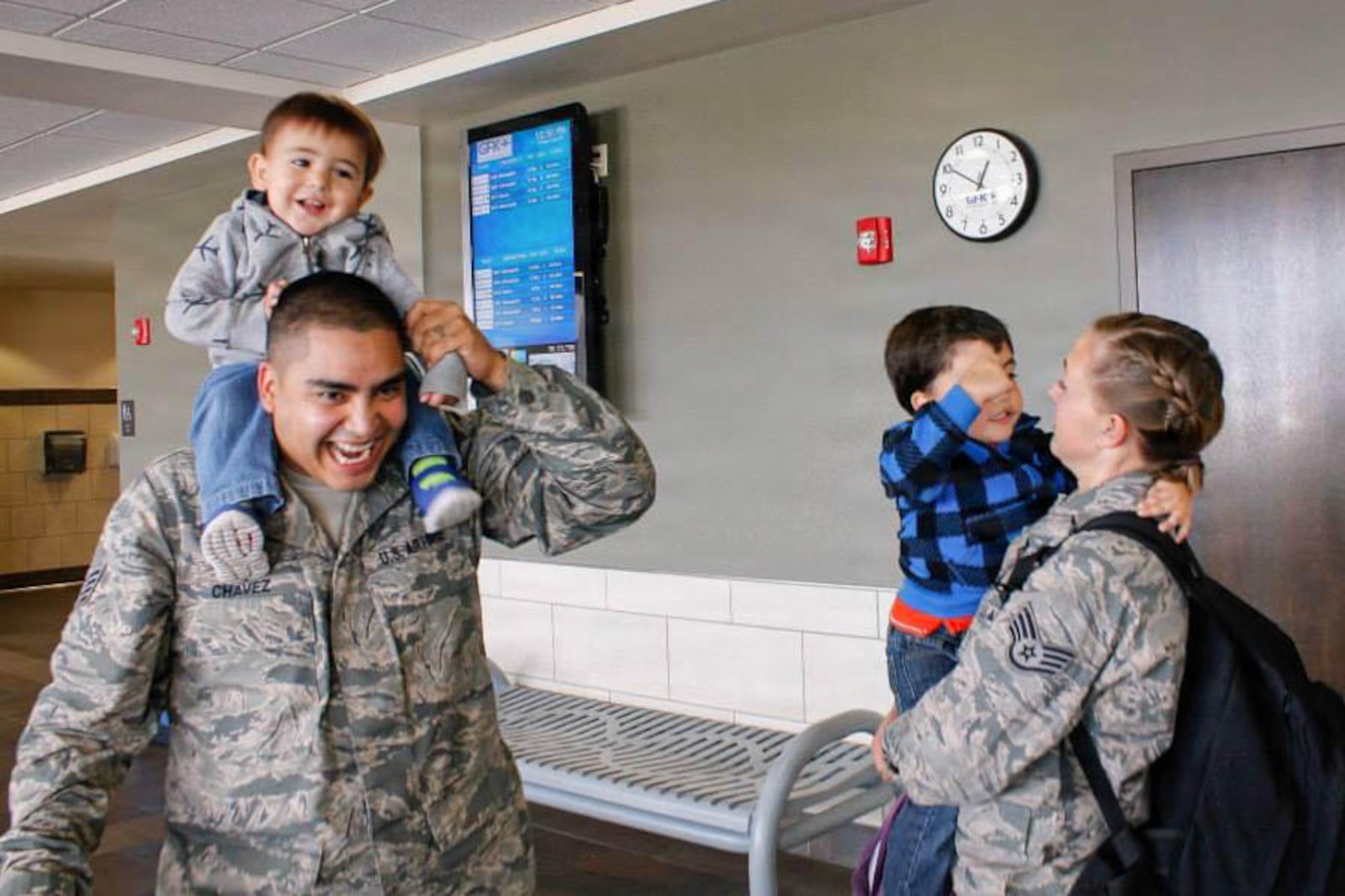 Two U.S. Airmen hold their young children in an airport.