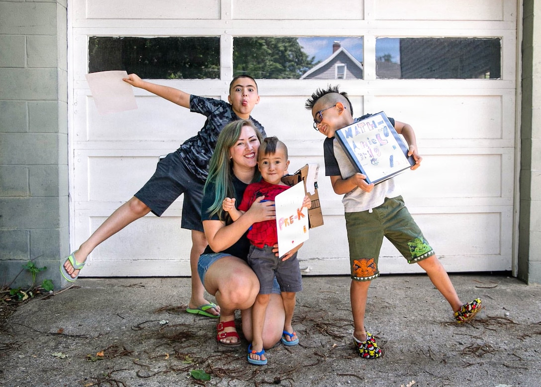 A woman poses with her three sons who are holding first day of school signs.
