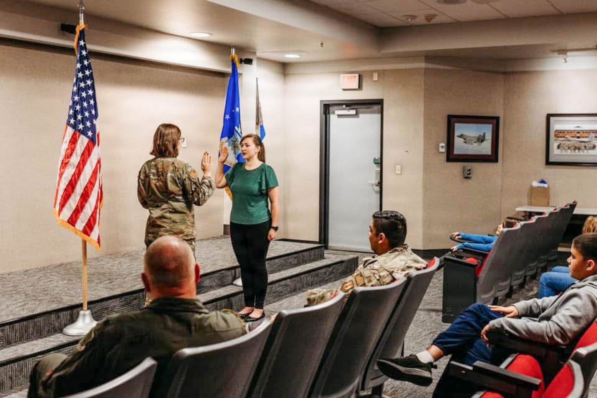 A woman raising her right hand to take an oath in front of an American flag, surrounded by friends.